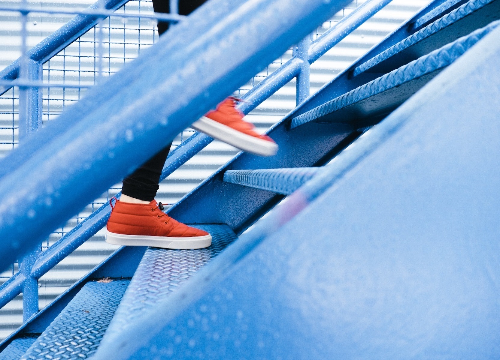 Vorankommen durch eigene Leistung - Person mit orangenen Schuhen, die zügig eine blaue Treppe hinaufsteigt